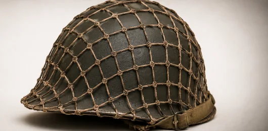 Historischer Stahlhelm mit Tarnnetz auf hellem Grund